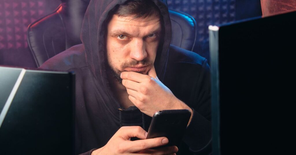 Golpista encapuzado usando smartphone, representando golpe e fraude no PIX